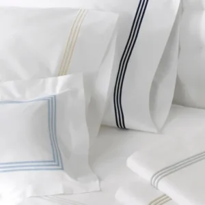 A collection of white bedding featuring various pillowcases and sheets adorned with pastel-colored decorative stripes. Featuring Bel Tempo Embroidered bedding by Matouk. Available at Linen Society.