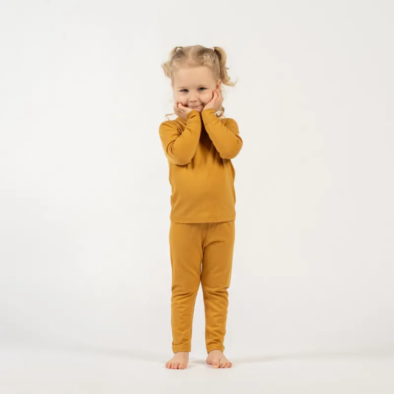 Young girl wearing a menique merino wool yellow long sleeve and bottom set on a white background